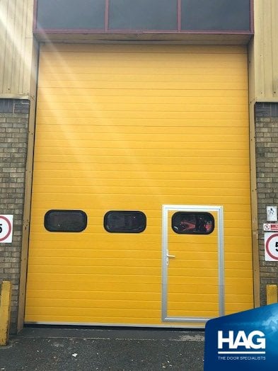 overhead sectional industrial door fitted with personnel door. Yellow powder coated.
